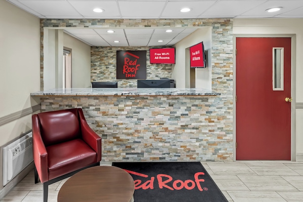 Una zona de recepción con pared de piedra, una puerta roja, un sillón de cuero rojo y un cartel que indica Wi-Fi gratuito en todas las habitaciones.