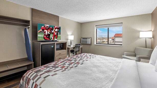 A hotel room with a bed, a desk, a TV, a window, and a view of the outside.