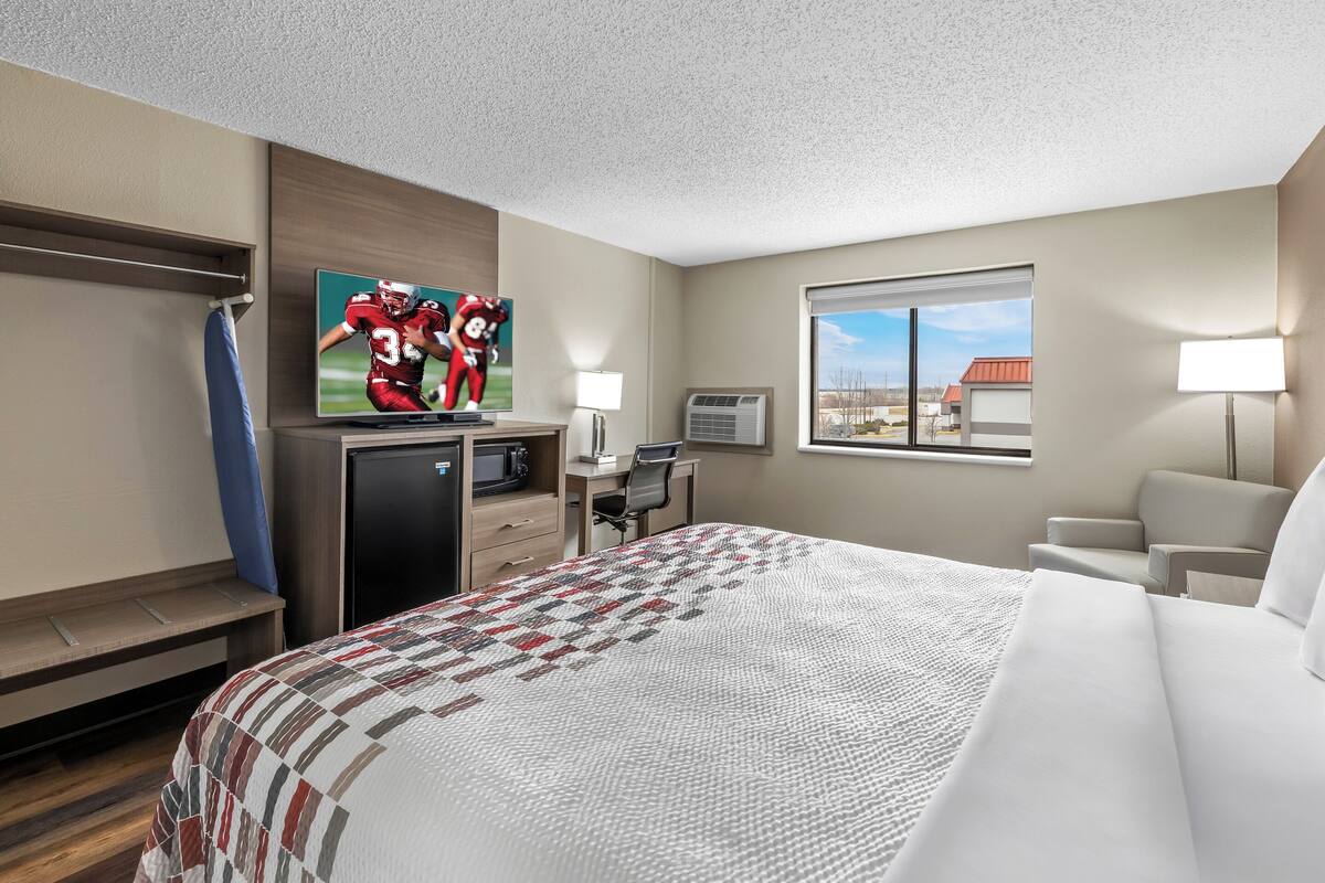 A hotel room with a bed, a desk, a TV, a window, and a view of the outside.