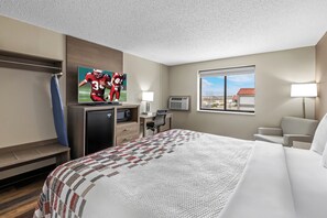 Habitación de hotel con cama, escritorio, televisión, ventana y vistas al exterior.