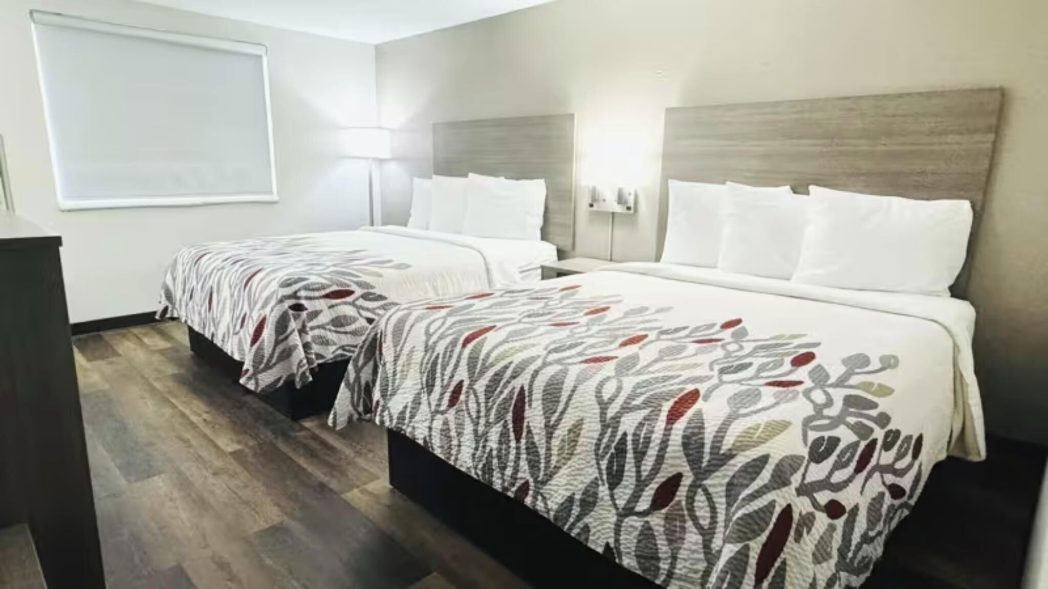 Hotellihuone, jossa on kaksi sänkyä, työpöytä ja suuri ikkuna.