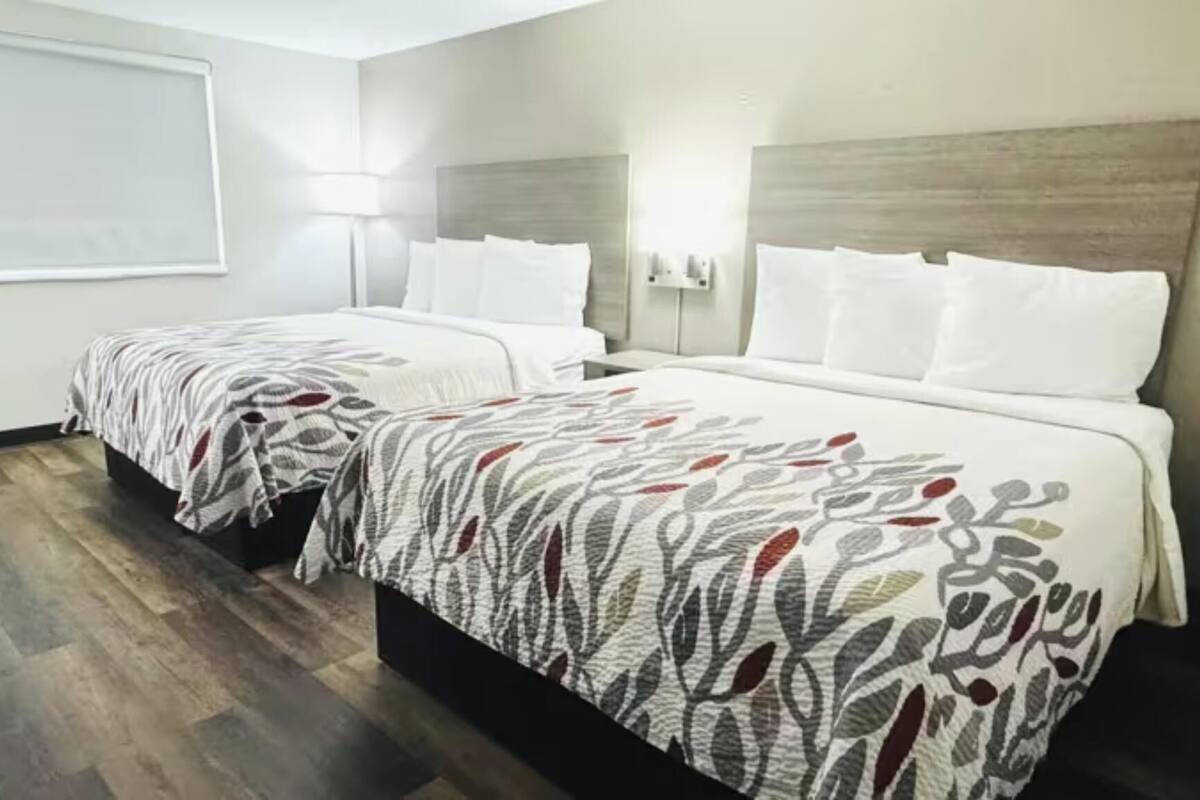 A hotel room with two beds, a desk, and a large window.