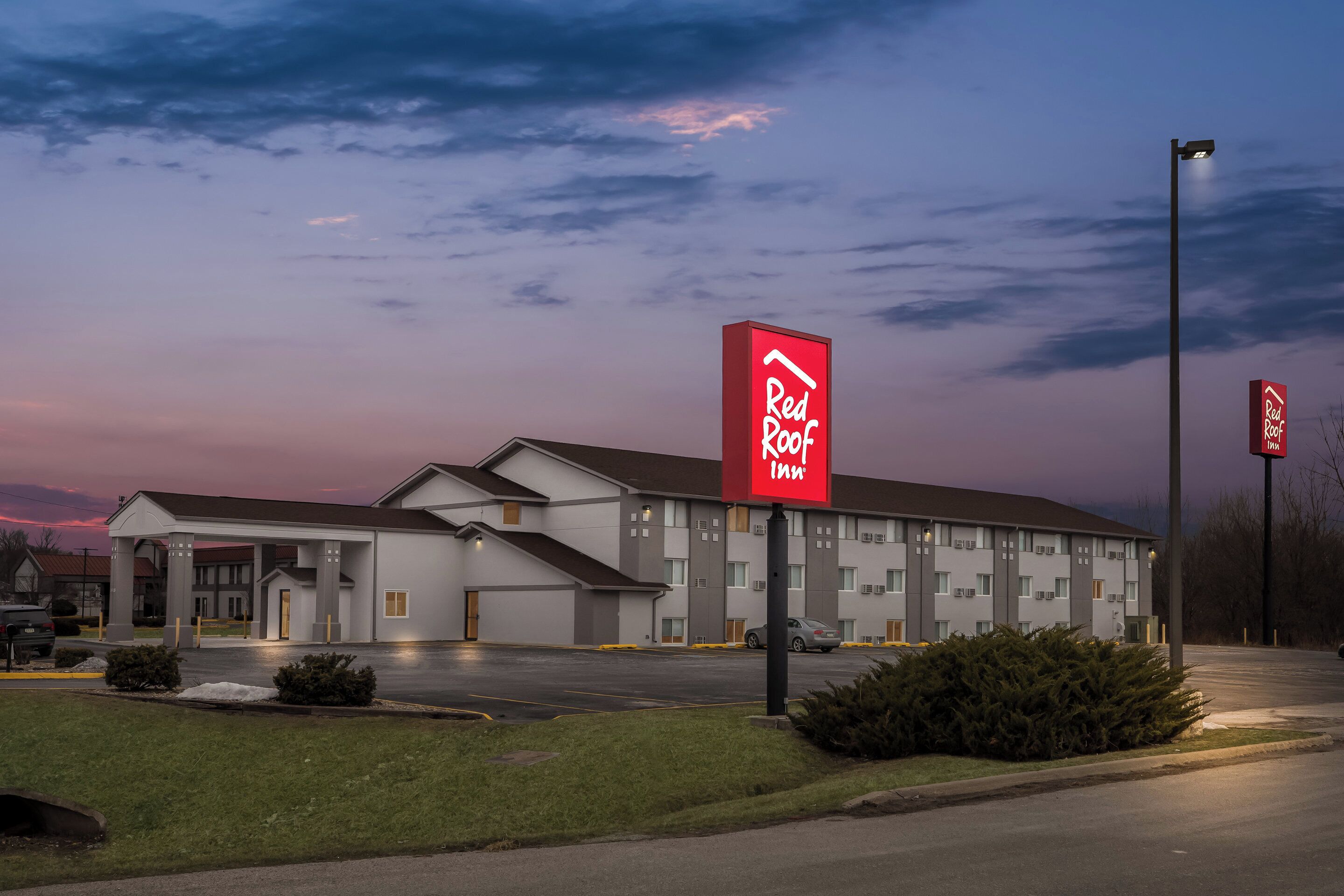 Een Red Roof Inn met een groot gebouw, een overdekte parkeerplaats en een verzorgd gazon.