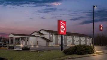 Een Red Roof Inn met een groot gebouw, een overdekte parkeerplaats en een verzorgd gazon.