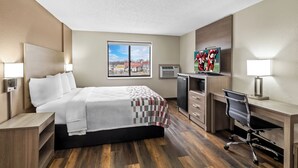 A hotel room with a bed, desk, chair, and a large window.