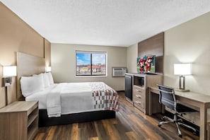 A hotel room with a bed, desk, chair, and a large window.