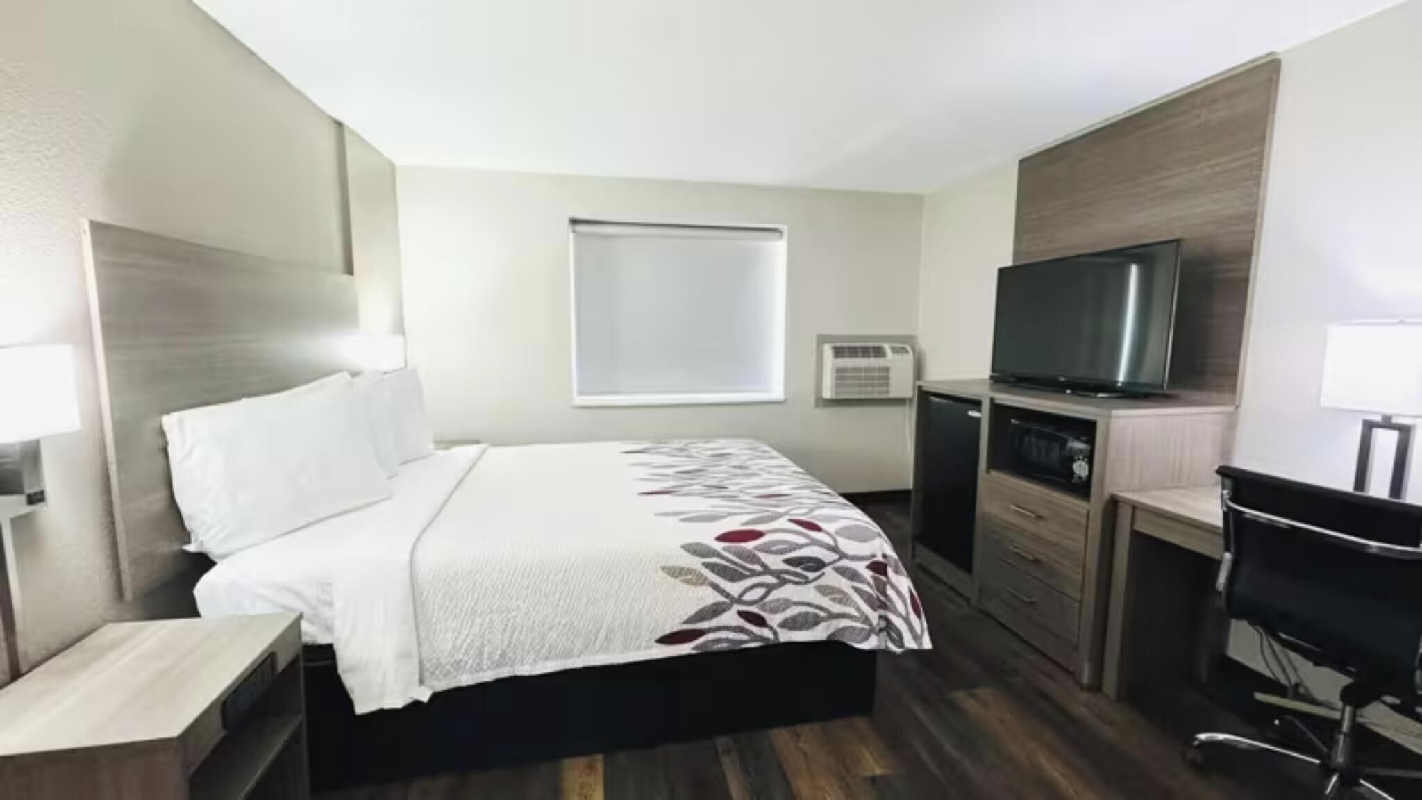 Hotellihuone, jossa on sänky, työpöytä, tuoli, televisio ja ikkuna.