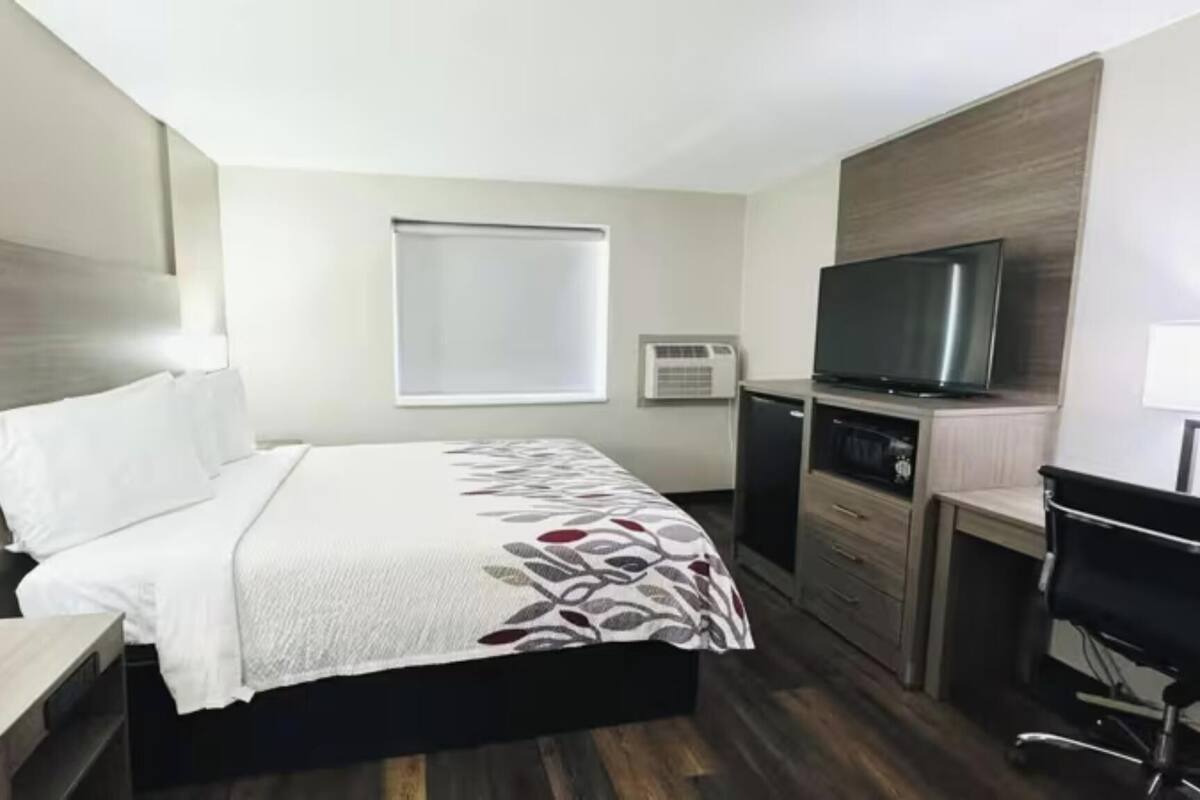 A hotel room with a bed, a desk, a chair, a television, and a window.