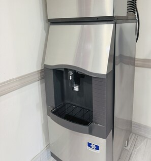 Dispensador de bebidas de acero inoxidable con sistema de vaso abatible y fuente de agua.