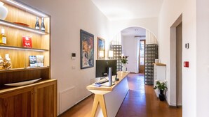 A hotel reception area with a wooden counter, a computer, and a desk lamp. There are shelves with bottles and a framed picture on the wall. - La Casa del Ghiberti B&B (Florence)