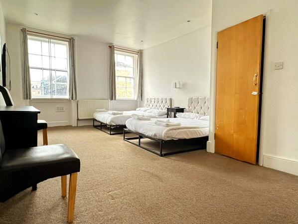 A hotel room with two beds, a wooden door, and a radiator.