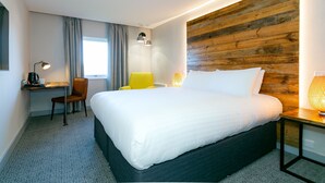 A modern hotel room with a large bed, a desk with a chair, a wooden accent wall, and a window with curtains. - Cedar Court Wakefield (Wakefield)