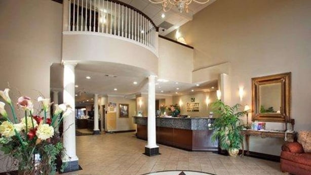 A hotel lobby with a reception desk, a glass coffee table, a star-patterned floor, and a staircase. - Quality Inn & Suites, Near University (Waco)