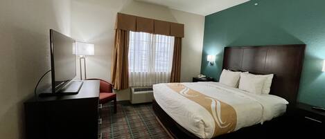 Hotelkamer met een bed, bureau, stoel, televisie, lamp en raam met gordijnen.