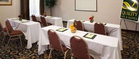 A conference room with tables set for meetings, a projector screen, and a sign for Quality Inn & Suites.