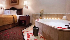 A hotel room with a bed, bedside table, lamp, and a large bathtub with rose petals on the floor. - Quality Inn & Suites, Near University (Waco)