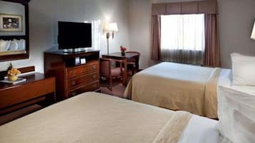 Habitación de hotel con dos camas, un escritorio con televisor, una lámpara y una ventana con cortinas.