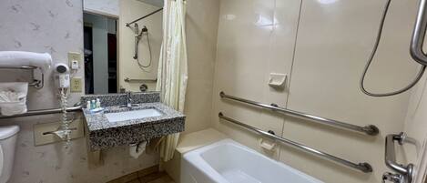 A bathroom with a white bathtub, a sink with a granite countertop, a handheld showerhead, and a towel rack.