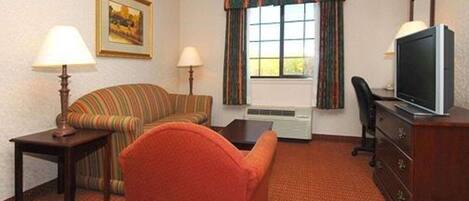 Une chambre d’hôtel avec un canapé à rayures, un fauteuil rouge, une télévision, un bureau et une fenêtre avec des rideaux.
