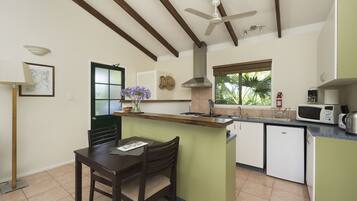 A kitchen with a dining area, wooden beams, a ceiling fan, a microwave, and a small refrigerator.