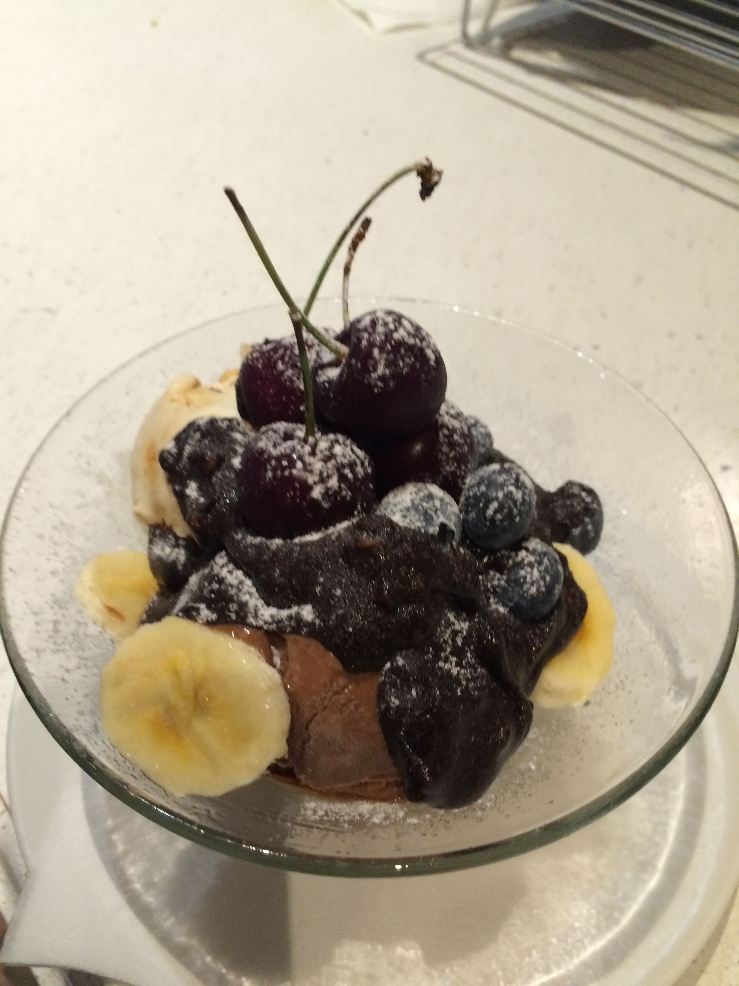 A dessert with cherries, blueberries, and banana slices in a clear glass bowl.