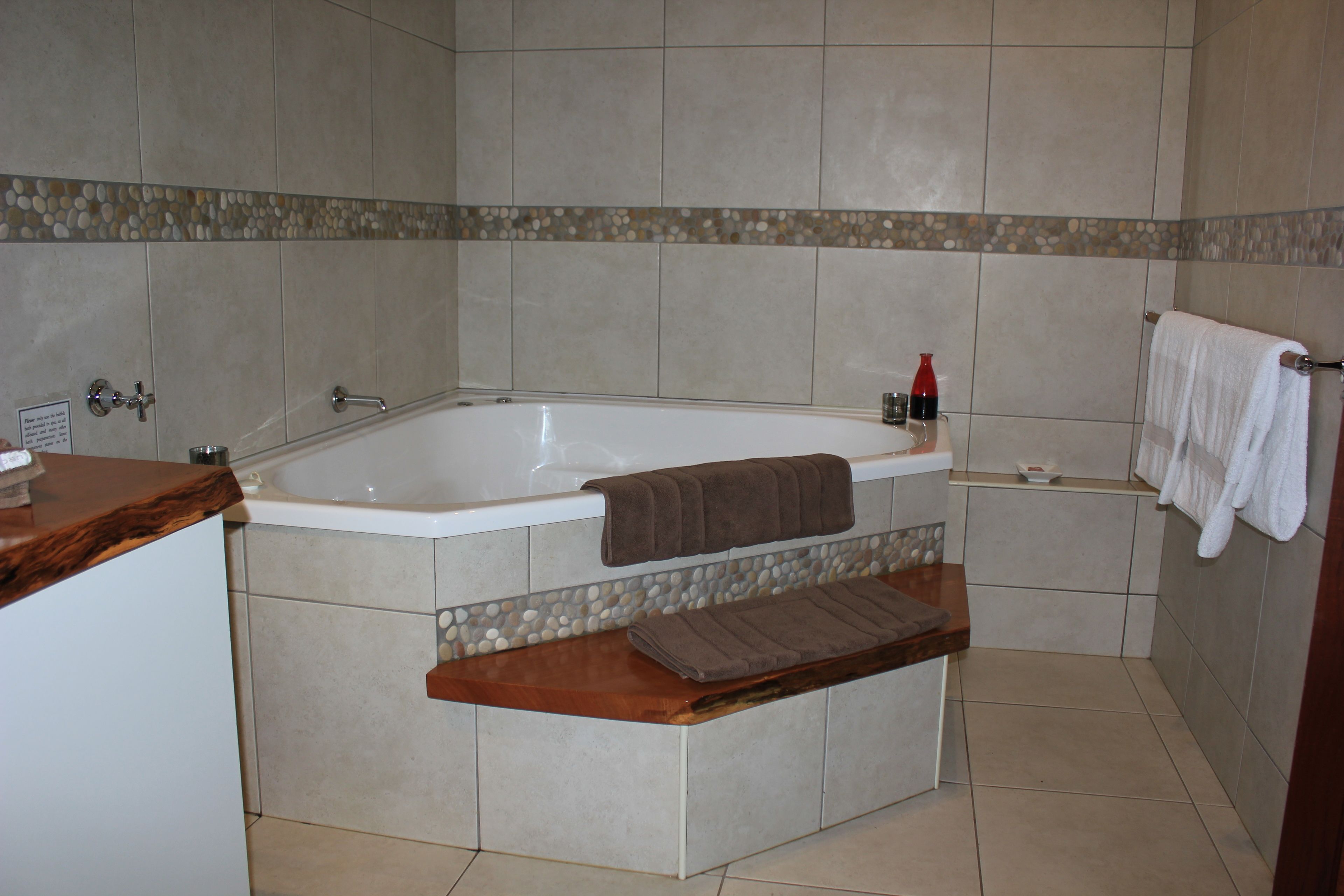 Une salle de bain avec une baignoire, une étagère en bois, un porte-serviettes et une petite table sur laquelle se trouve une bouteille.