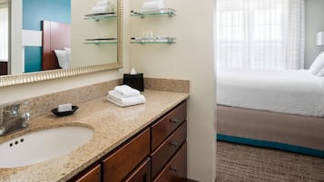 A hotel bathroom with a granite countertop sink, a mirror, and glass shelves above the sink.