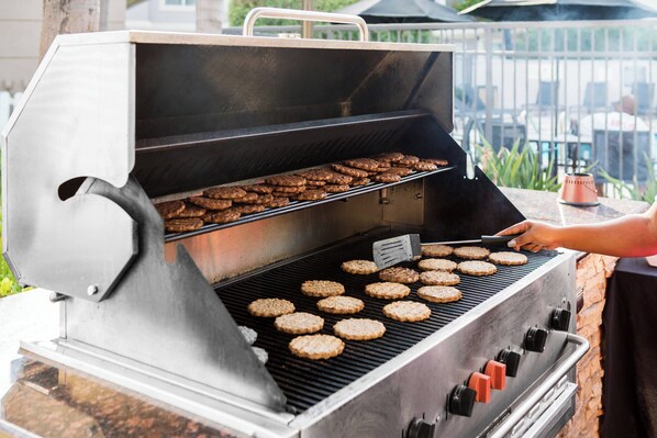 A stainless steel grill with multiple cooking levels and a side burner, used for grilling hamburgers.