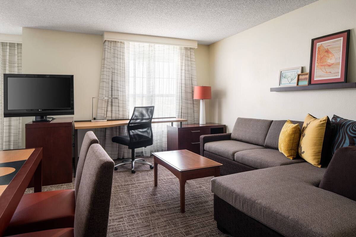 A hotel room with a sofa, a desk, a television, a chair, and a lamp.