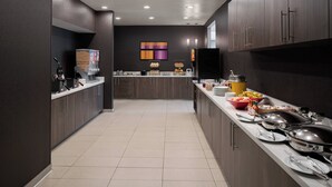 A modern kitchen with dark wood cabinets, a long countertop with various food items, and a central island with a sink. - Residence Inn by Marriott Cypress Los Alamitos (Los Alamitos)