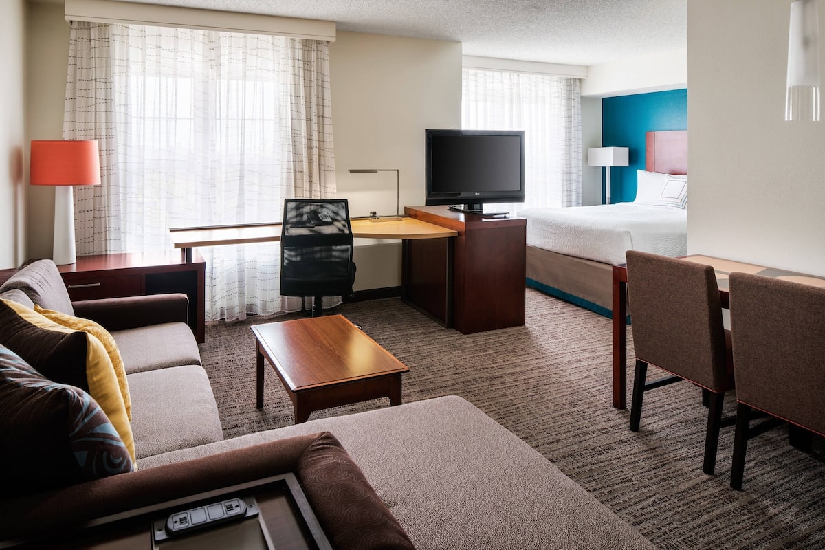 A hotel room with a sofa, a desk with a TV, a bed, and a small table.
