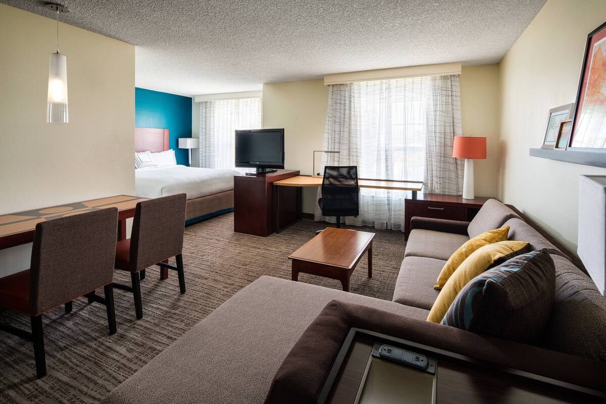 A hotel room with a bed, desk, TV, and seating area.