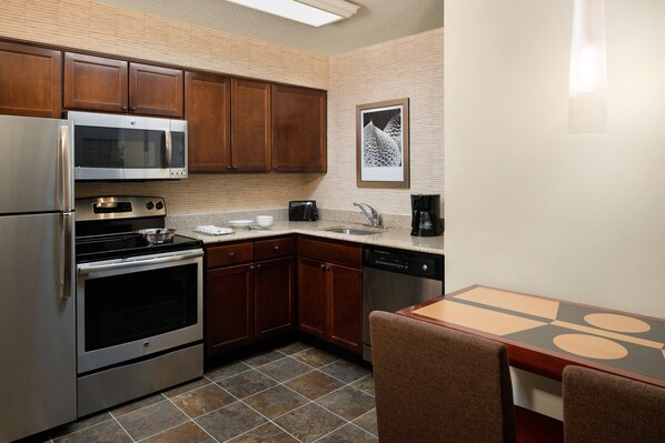 A kitchen with wooden cabinets, stainless steel appliances, a tiled floor, and a dining area with a table and chairs.