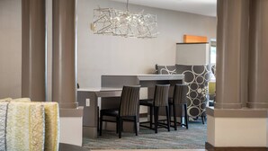 A modern hotel room with a dining area featuring a table and chairs, a patterned rug, and a unique hanging light fixture. - Residence Inn by Marriott Cypress Los Alamitos (Los Alamitos)