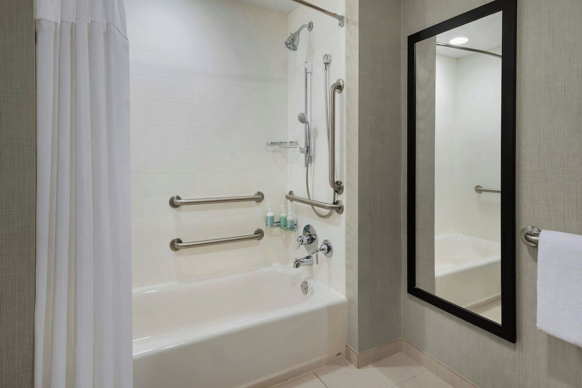 A modern bathroom with a bathtub, shower, and handrails.
