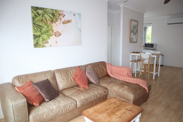 A living room with a brown leather sofa, a wooden coffee table, and a painting of a beach scene. - Coolum Beach Resort (Coolum Beach)