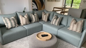 Un sofá modular con almohadones a rayas, un reposapiés redondo y un control remoto encima.