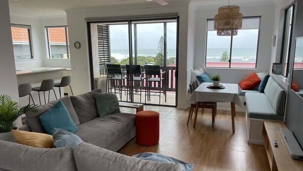 Una sala de estar moderna con un sofá gris, una mesa de comedor y un balcón con vistas al océano.