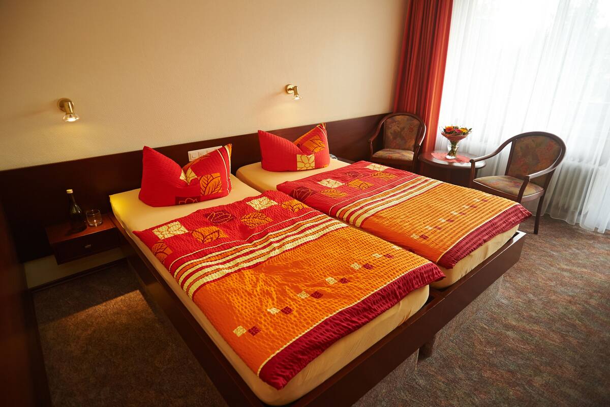 A hotel room with two beds, a nightstand, a chair, and a small table with a vase of flowers.