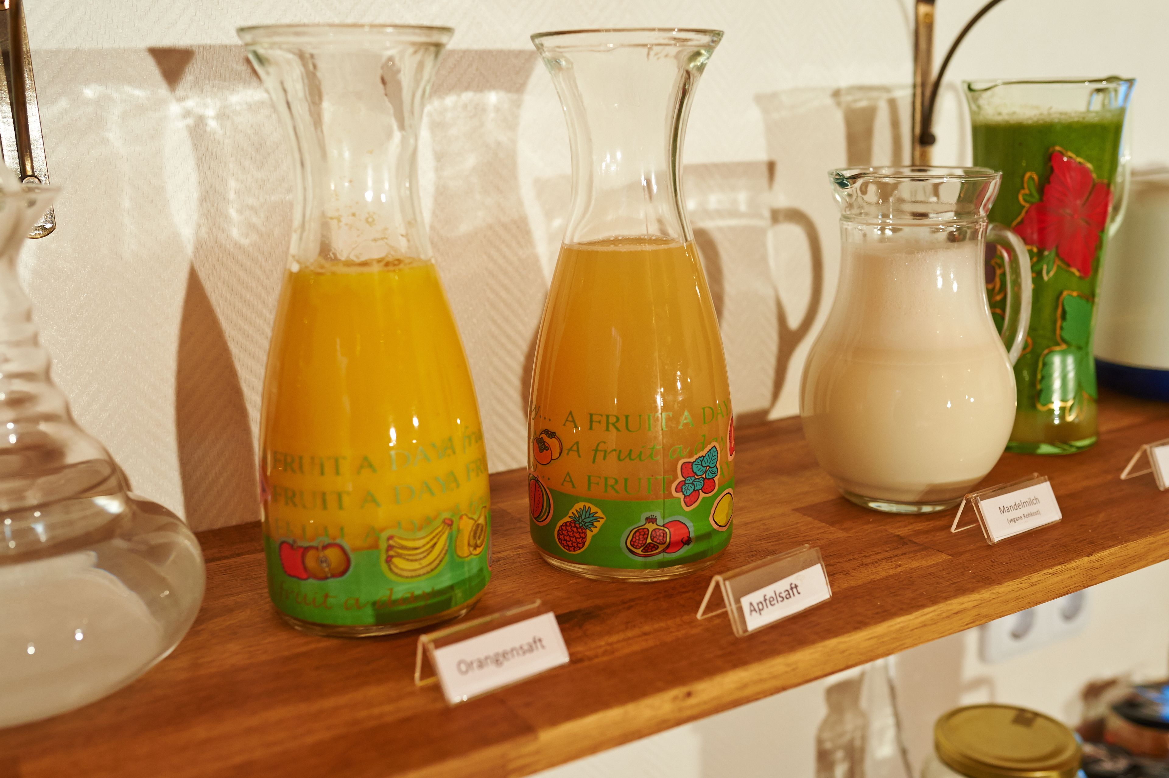 A wooden shelf with three glass bottles labeled with different fruit juices.