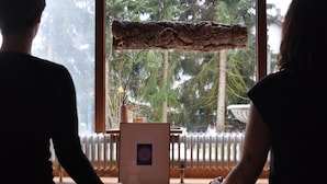Dos personas sentadas en un tapete mirando una ventana con una viga de madera encima.