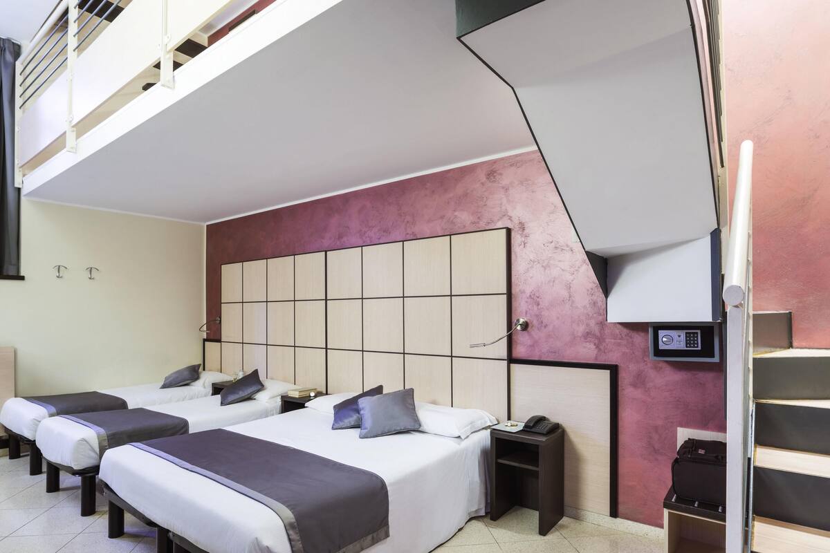 A hotel room with two beds, a built-in headboard, a bedside table with a phone, and a small shelf.