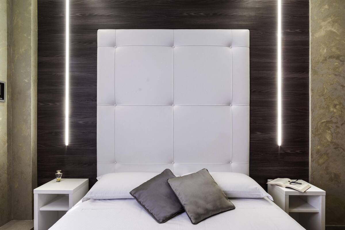 A modern bedroom with a tufted headboard, bedside tables, and a nightstand with a book and glasses.