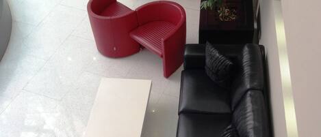 Una sala de estar moderna con un sofá de cuero negro, un sillón rojo y una mesa de centro blanca.