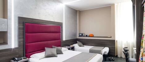 Habitación de hotel con dos camas, un cabecero rojo grande, una mesita de noche con un teléfono y una mesa pequeña con una radio y un bolso.