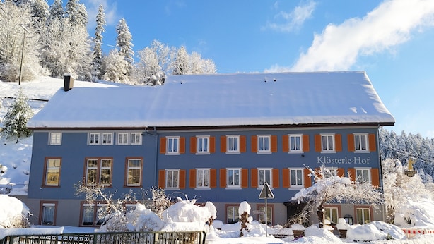 Un edificio grande de dos pisos con fachada azul y contraventanas naranjas, rodeado de árboles cubiertos de nieve y un cielo despejado.
