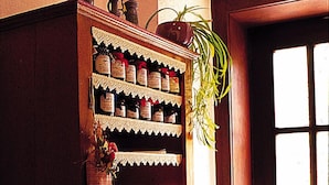 Un armario de madera con varios estantes, cada uno con botellas y frascos. Una cesta de mimbre con flores está sobre una mesita auxiliar junto al armario.