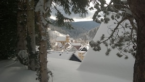 Un pueblo cubierto de nieve con edificios tradicionales, rodeado de árboles y montañas.