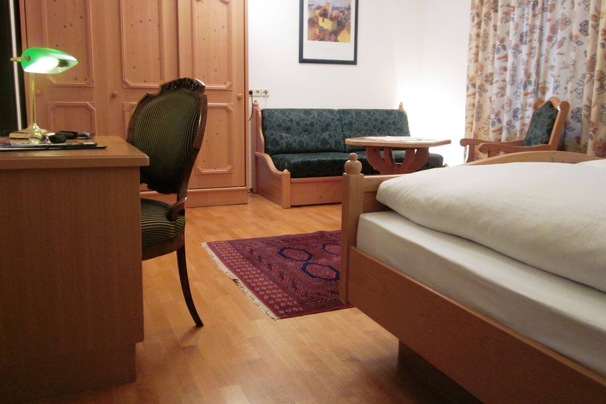 Una habitación con un escritorio de madera, un sofá verde, una cama y una pequeña mesa.