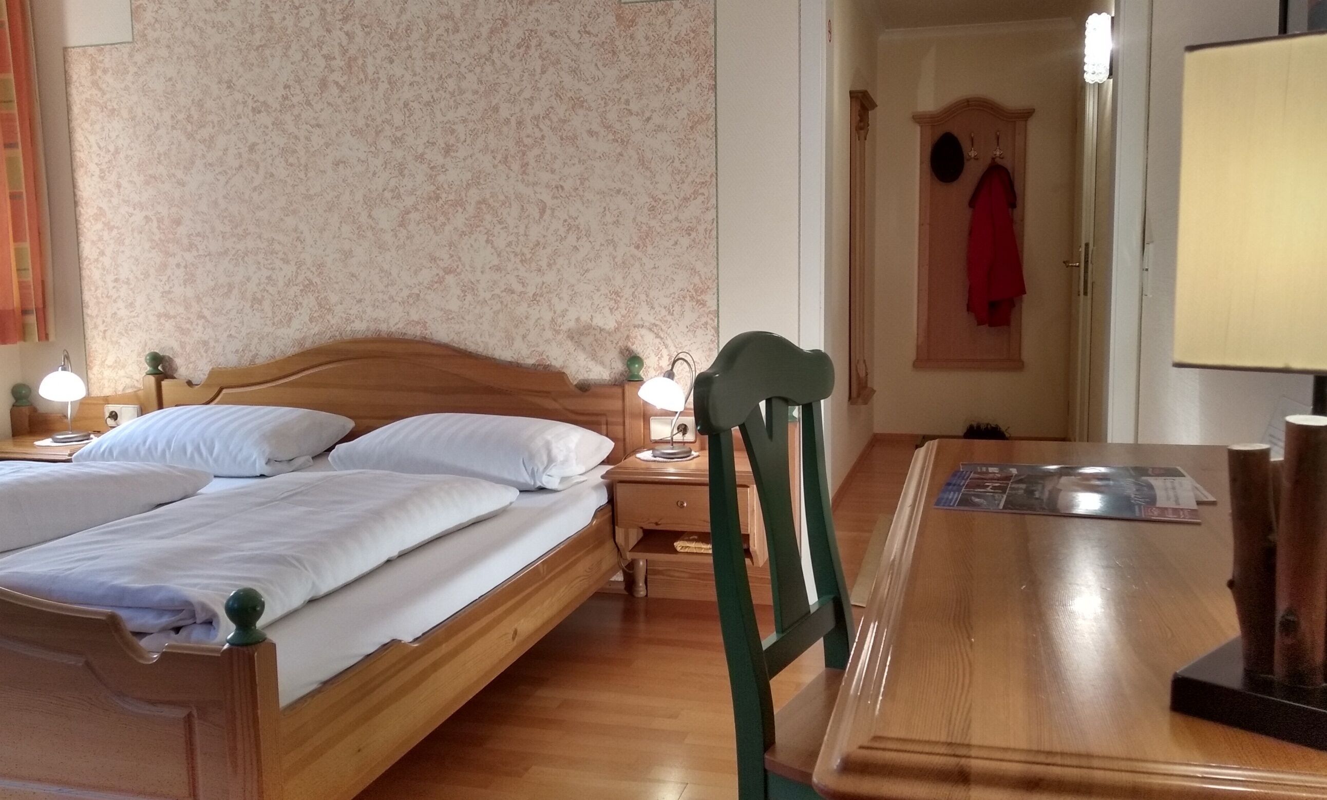 A hotel room with two wooden beds, a wooden desk, and a chair.
